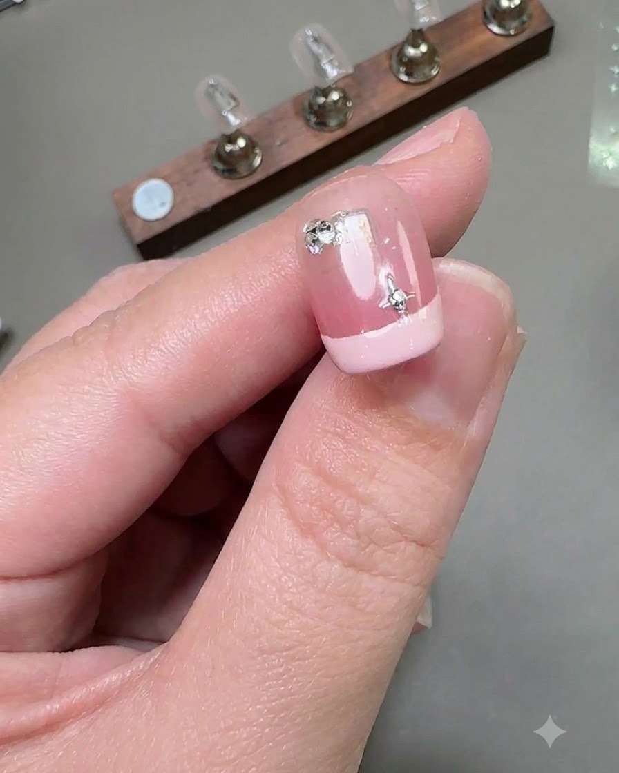 Nahaufnahme eines kurzen French-Nogels mit einem silbernen Sternaufkleber und einem kleinen runden Diamanten in der Nagelbett-Gegend.