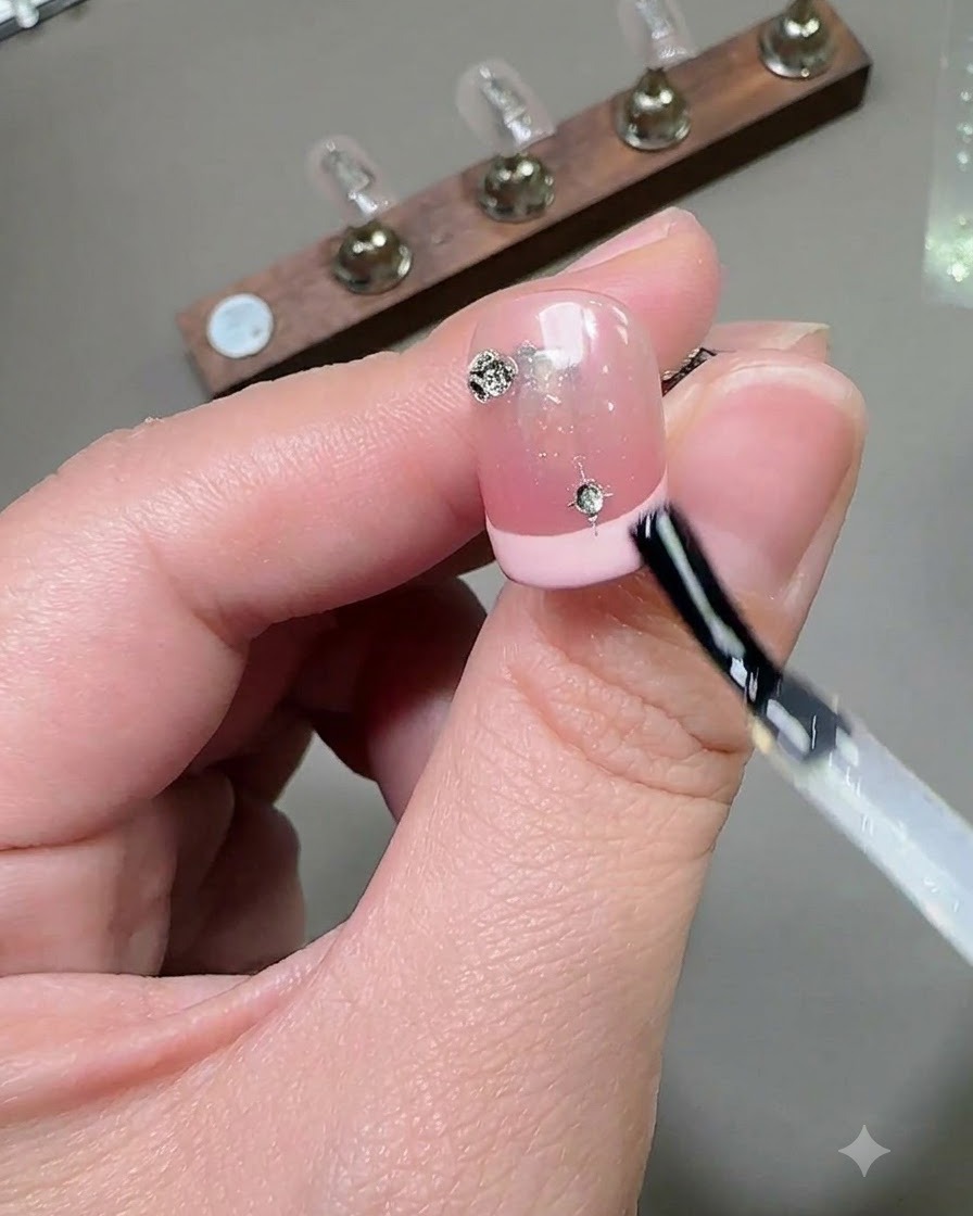 Ein Pinsel trägt eine glänzende Top-Coat-Schicht über einen verzierten Nagel mit Strasssteinen und Stern-Charms auf.
