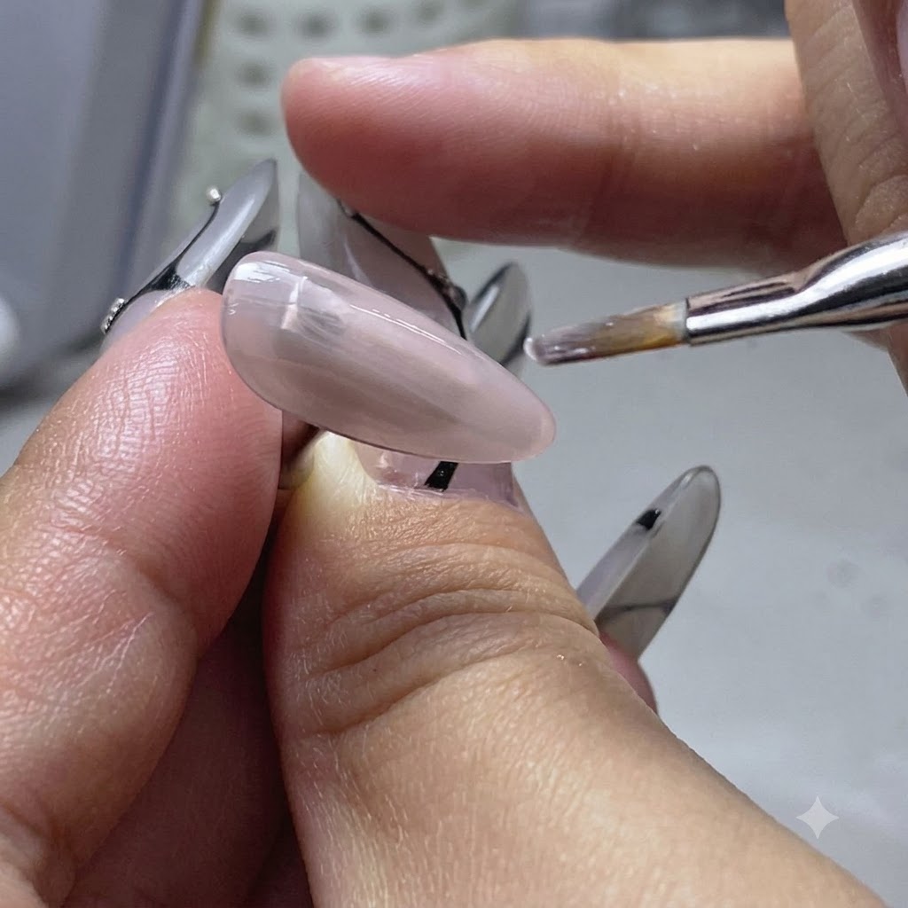 Ein Flachpinsel trägt eine dünne Schicht Nude-Base-Gel auf einen Übungsnagelfinger auf.