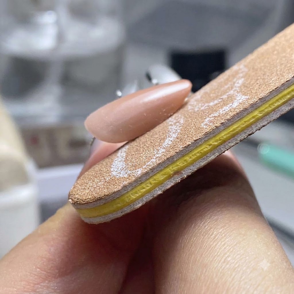 Eine Nagelfeile formt und glättet die drei Seiten eines fertigen Gelnagels.