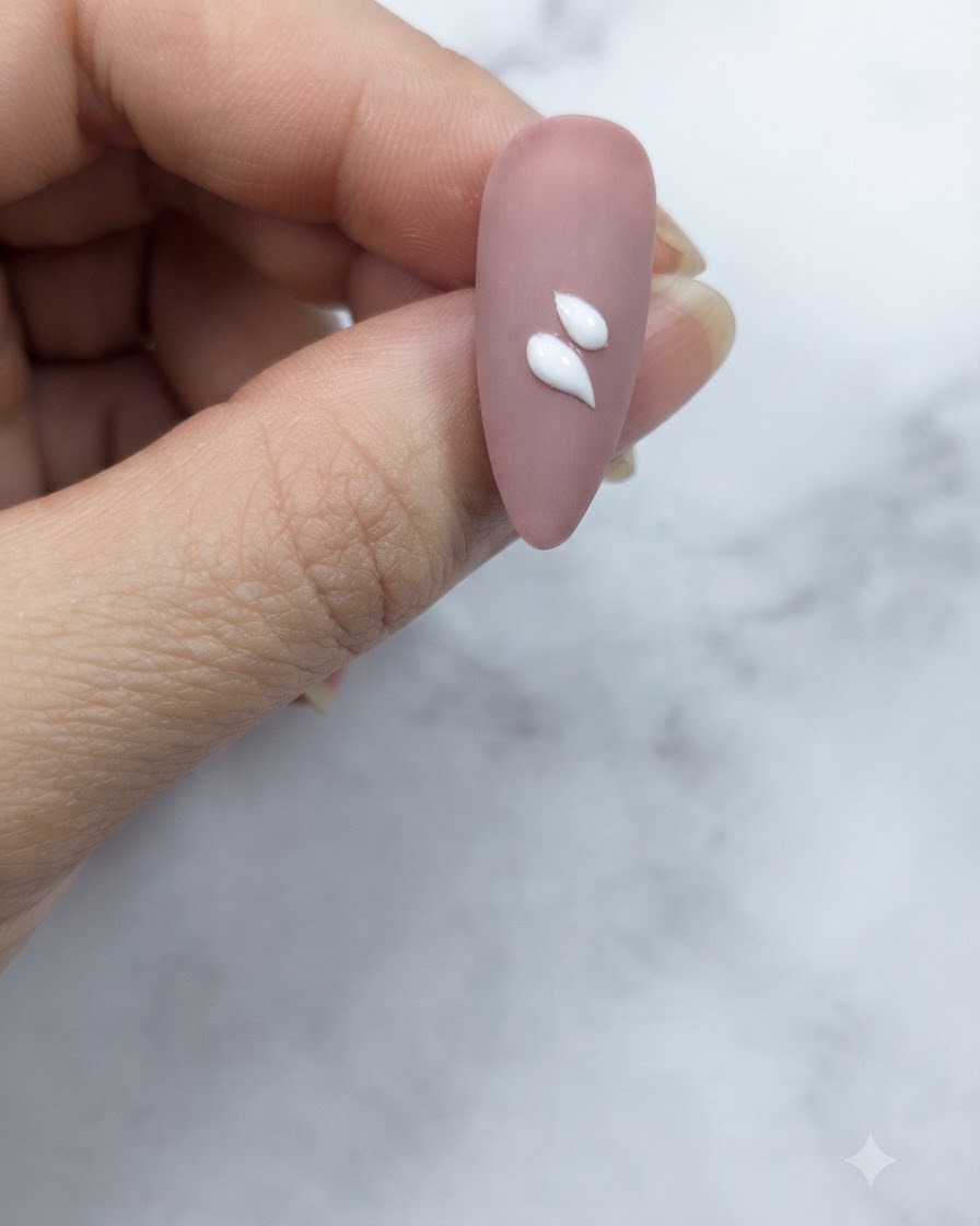Eine Nahaufnahme eines rosafarbenen Nude-Nagels mit zwei markanten weißen, tropfenförmigen Blütenblattstrichen nahe der Mitte.