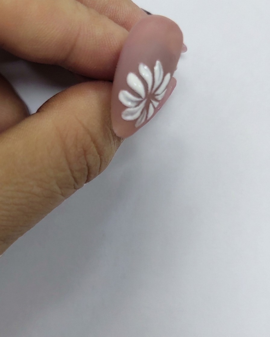 Eine aufgemalte weiße Gänseblümchenblüte auf einem Nagel mit einem winzigen gelben Punkt präzise in der Mitte.