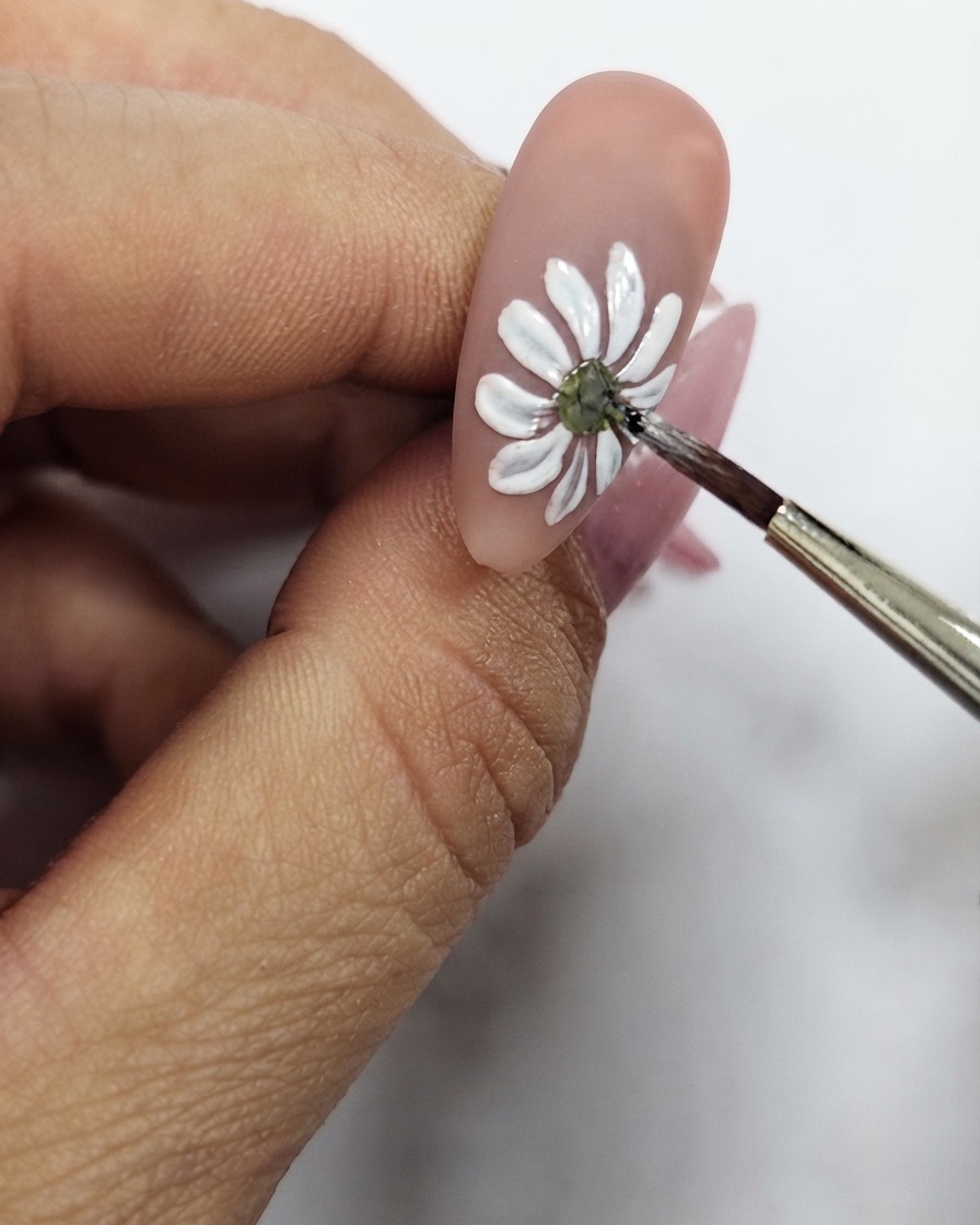 Eine Nahaufnahme eines feinen Pinsels, der den gelben Mittelpunkt der weißen Gänseblümchen-Nail-Art verfeinert.