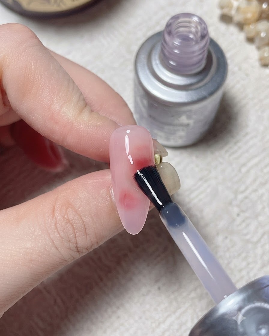 Ein Pinsel trägt eine Top-Schicht über ein ausgehärtetes Nageldesign mit einer silbernen Flasche im Hintergrund auf.