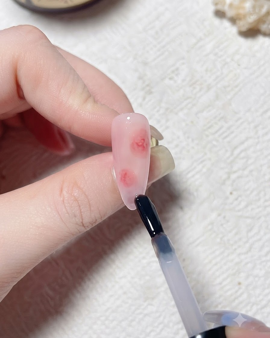 Ein Pinsel trägt eine klare Schicht Blooming Gel auf einen künstlichen Nagel mit Rosaton auf.