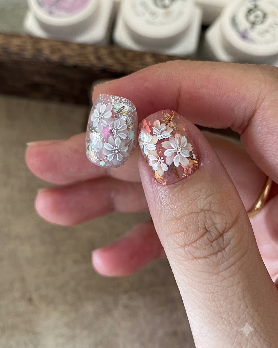 Eine Nahaufnahme eines Nageldesigners, der mit einem kleinen Schwamm farbiges Gel auf das Zentrum der weißen Blumen-Nail-Art aufträgt.