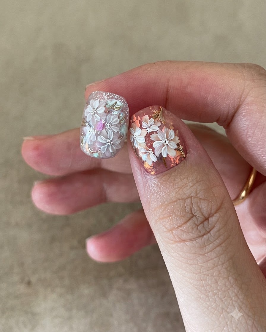 Ein Nagelpinsel trägt einen klaren Top Coat über komplizierte Blumen- und Goldfolien-Nagelkunst auf.