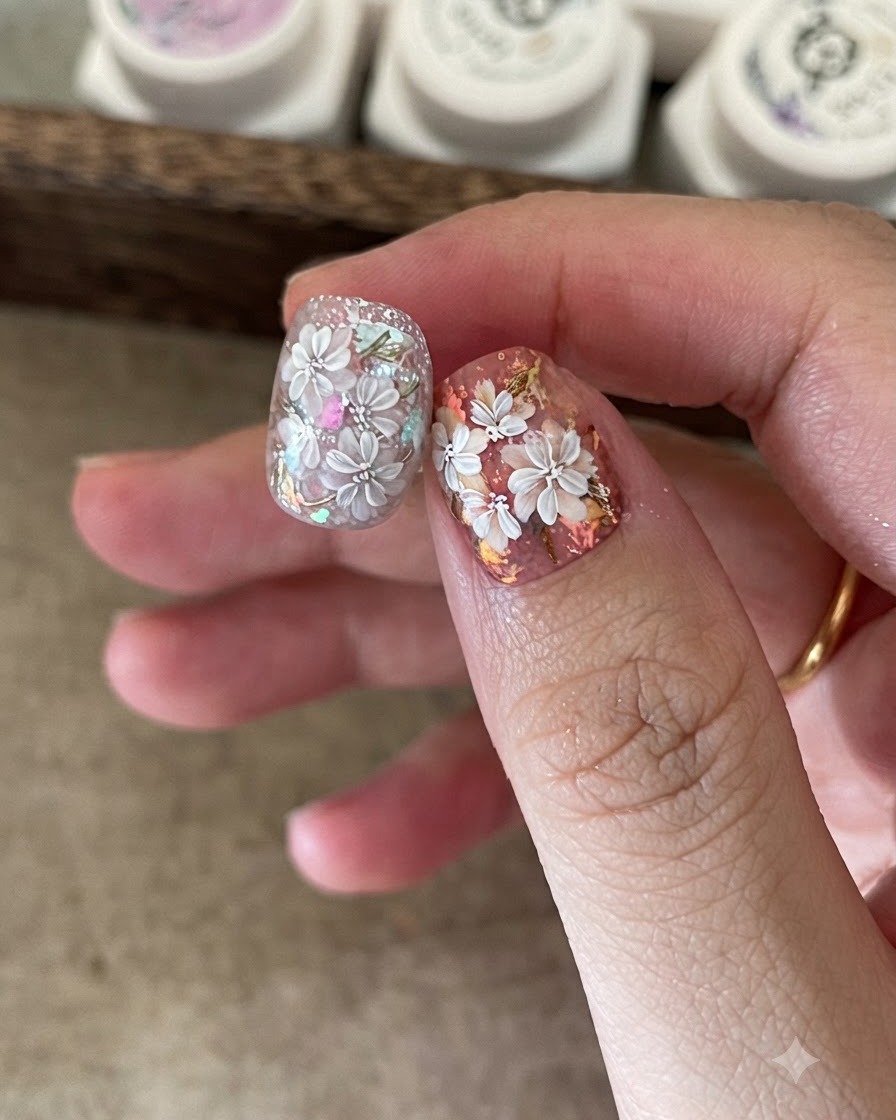 Ein feiner Nail-Art-Pinsel fügt detaillierte weiße Blütenblätter über ein vorgemaltes florales Nageldesign hinzu.