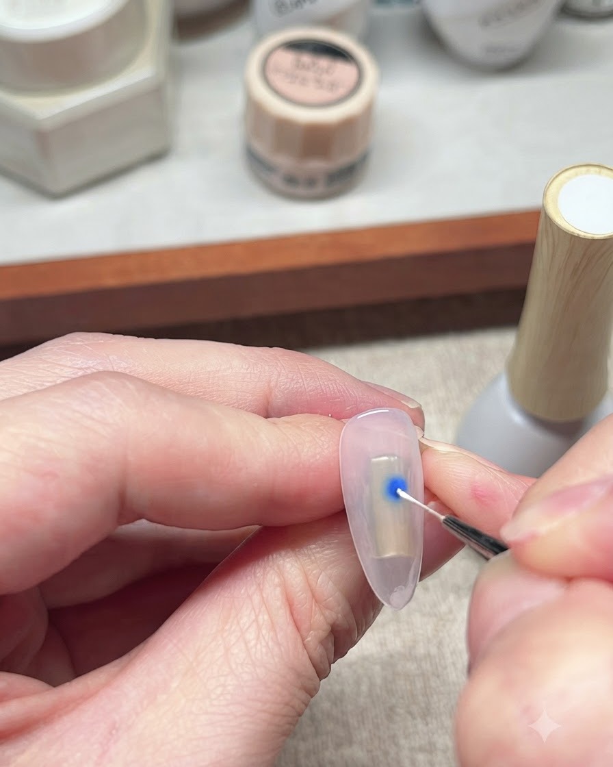 Ein feiner Liner-Pinsel interagiert mit einem blauen Gel-Lack-Punkt auf einem Nagel, um den Verlaufseffekt zu starten.