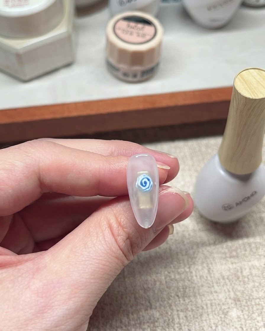 Nahaufnahme eines fertigen blauen Rosen-Gel-Nageldesigns neben einer weißen Flasche Nagelprodukt.