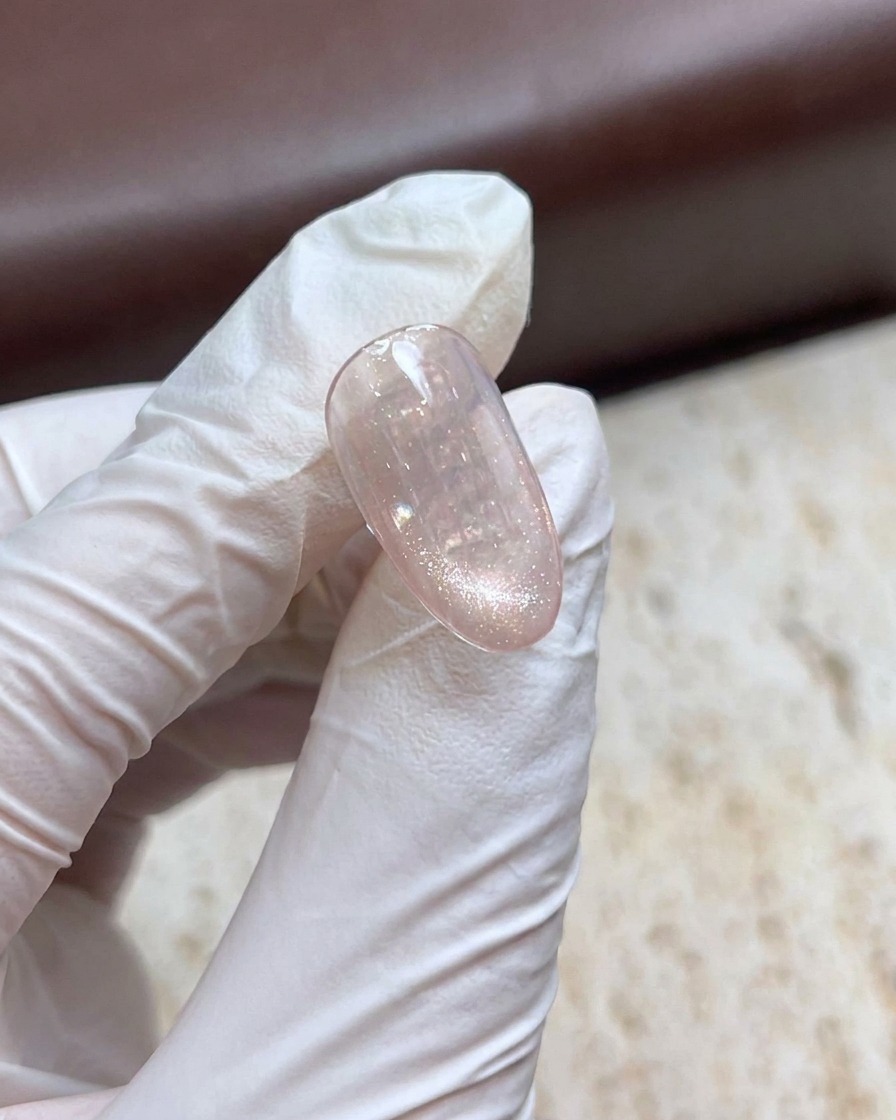 Eine behandschuhte Hand hält einen Magnetstab über einen schimmernden Cat-Eye-Gel-Nagel, um einen Perleneffekt zu erzeugen.