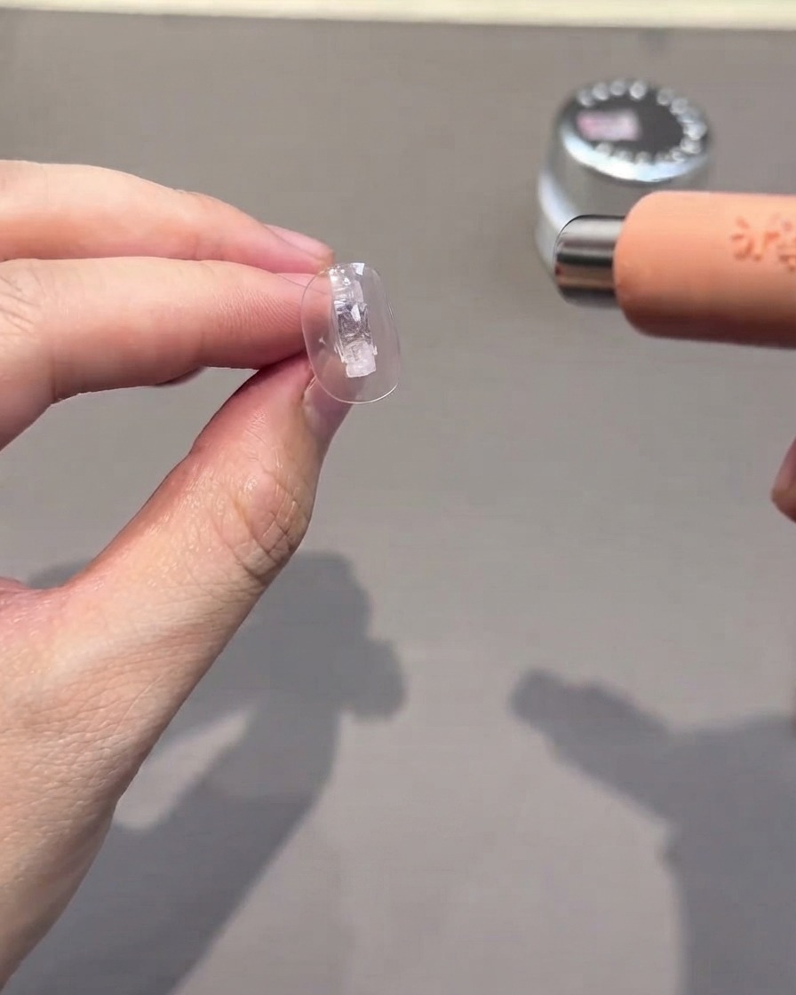 Eine klare Nagelspitze wird unter einer kleinen tragbaren UV- und LED-Lampe ausgehärtet.