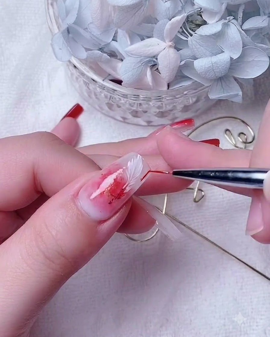 Nahaufnahme einer Nail-Designerin, die einen dünnen Detailpinsel verwendet, um rotes Gel auf einem milchweißen Basisnagel zu verblenden.