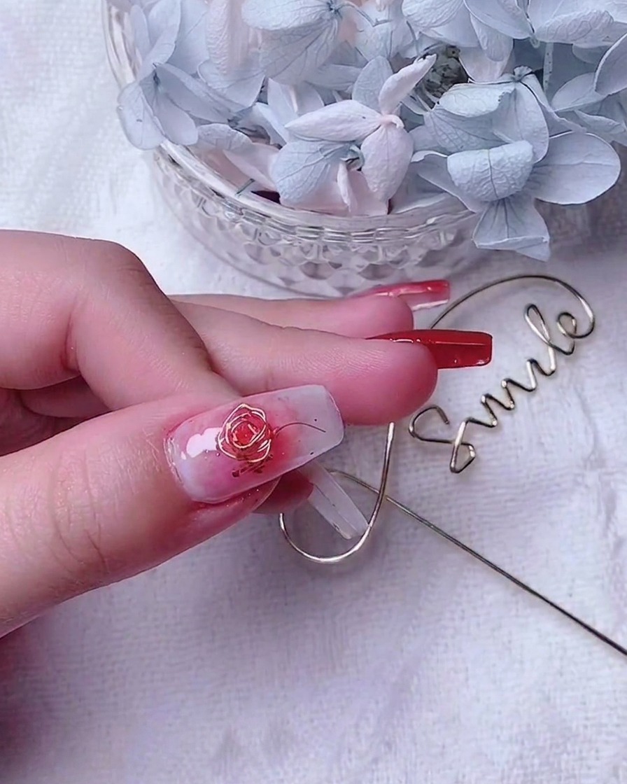 Nahaufnahme eines verzierten Daumennagels mit einer Golddraht-Rose und kleinen Akzentspendern am Rand.