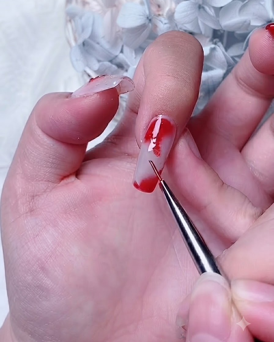 Ein Detailpinsel trägt rotes Gel auf eine Blooming-Gel-Schicht an der Ecke eines Zeigefingernagels auf.