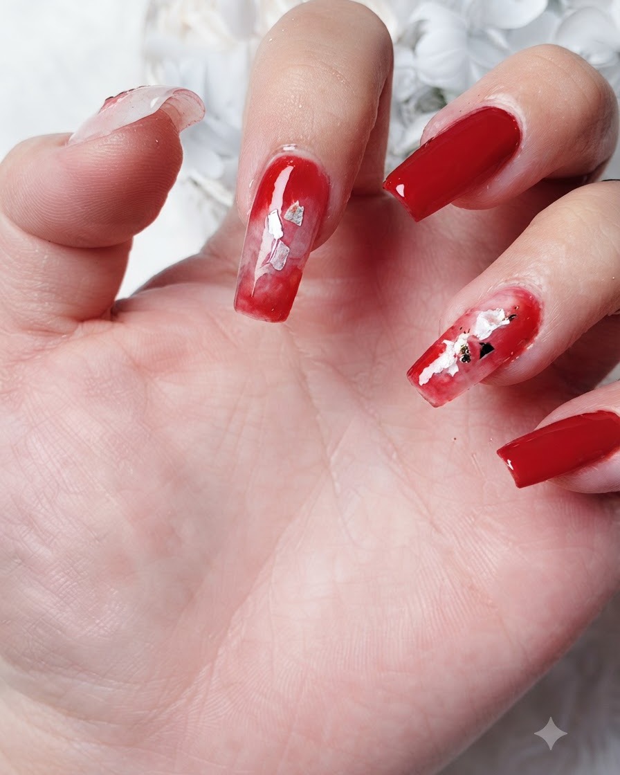 Nahaufnahme von kleinen, blattförmigen Goldfolienstücken, die in einen verlaufenden roten Blooming-Gel-Bereich auf einem Fingernagel eingesetzt werden.