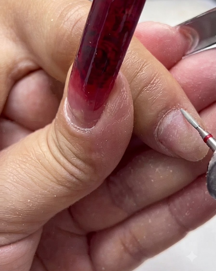 Eine elektrische Nagelfeile mit einem Keramik-Sicherheitsbit, die den Nagelhautbereich eines Naturnagels bearbeitet.