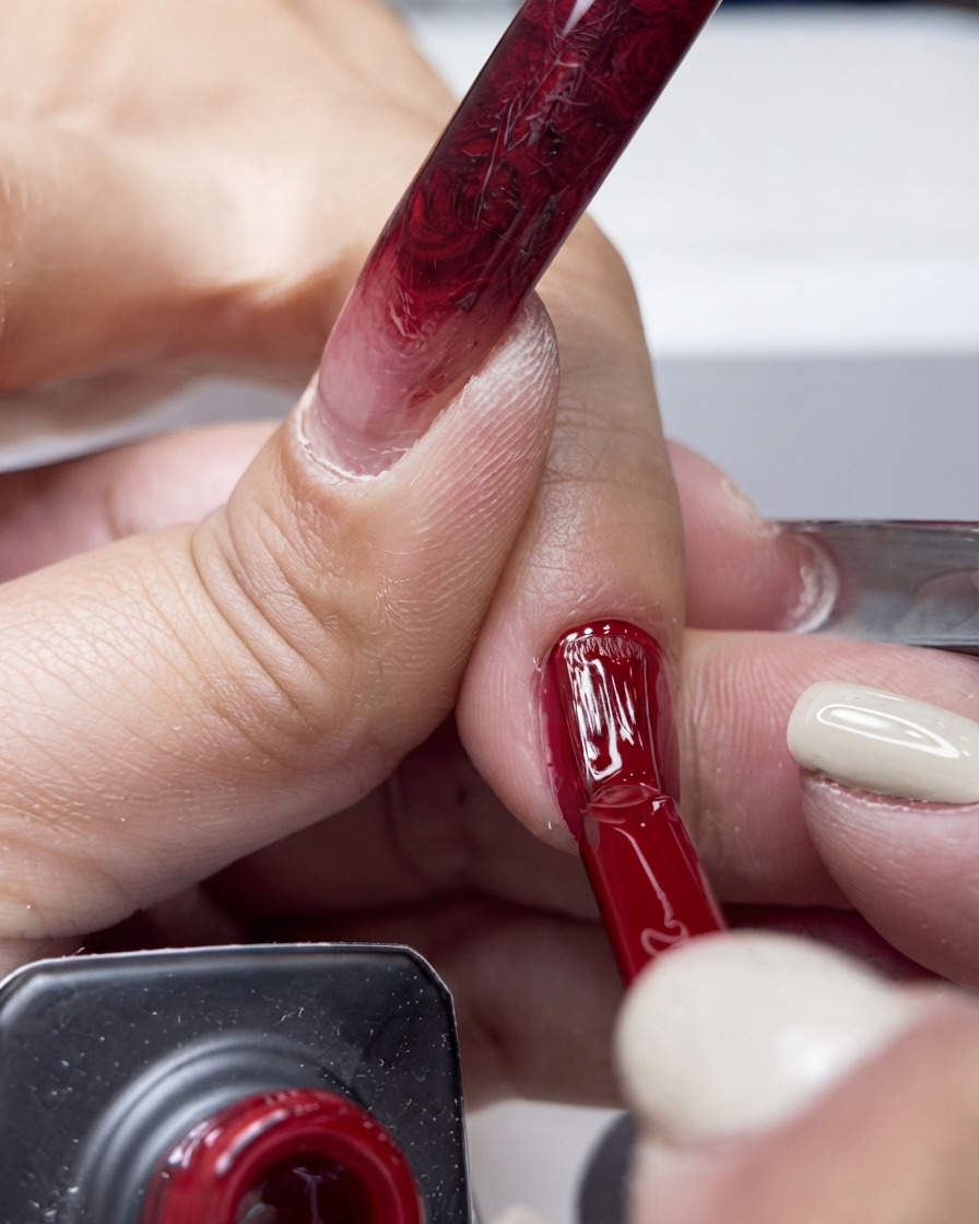 Ein Pinsel trägt einen lebendigen roten Gel-Nagellack in die Mitte eines Fingernagels auf.
