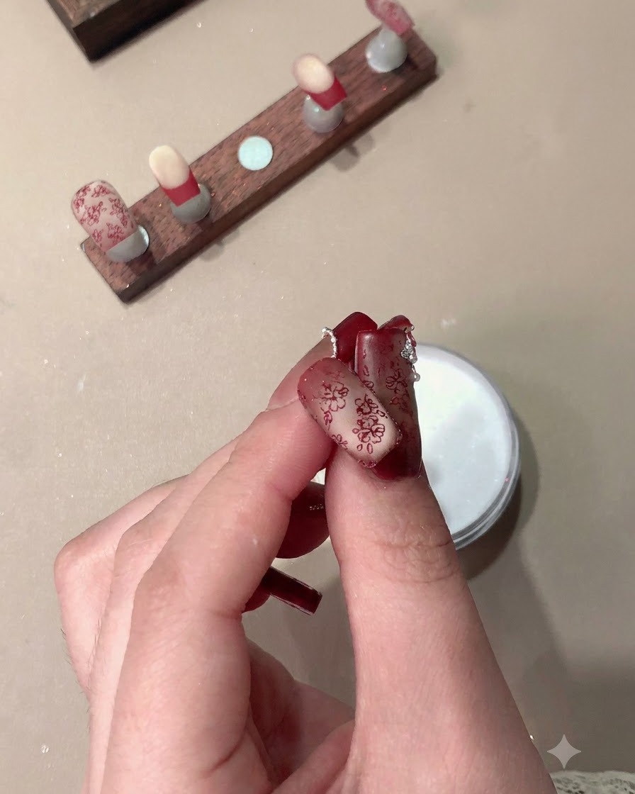 Eine Hand hält fertige Press-on-Nägel mit roten Stamping-Mustern und French-Spitzen.