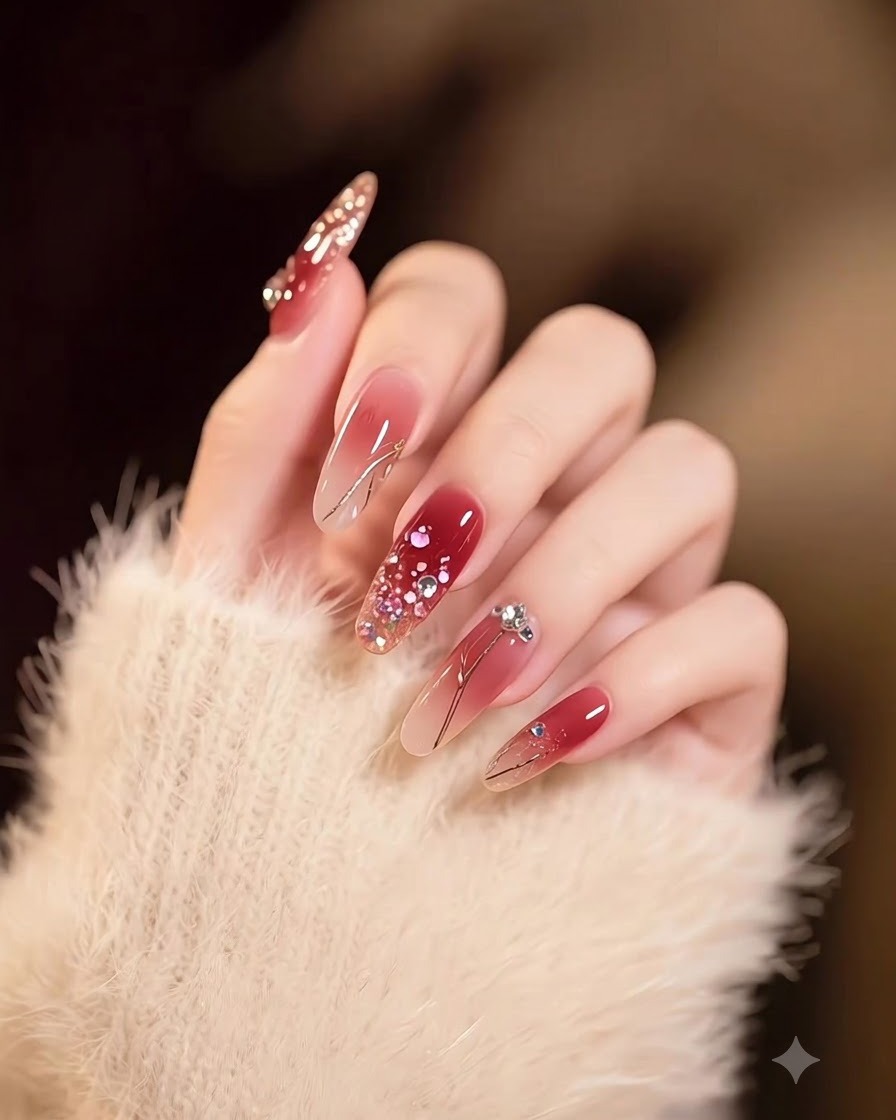 Eine Hand mit langen, quadratischen Nägeln mit einem sanften Verlauf von Nude zu tiefem Burgund, dekoriert mit Goldflocken.