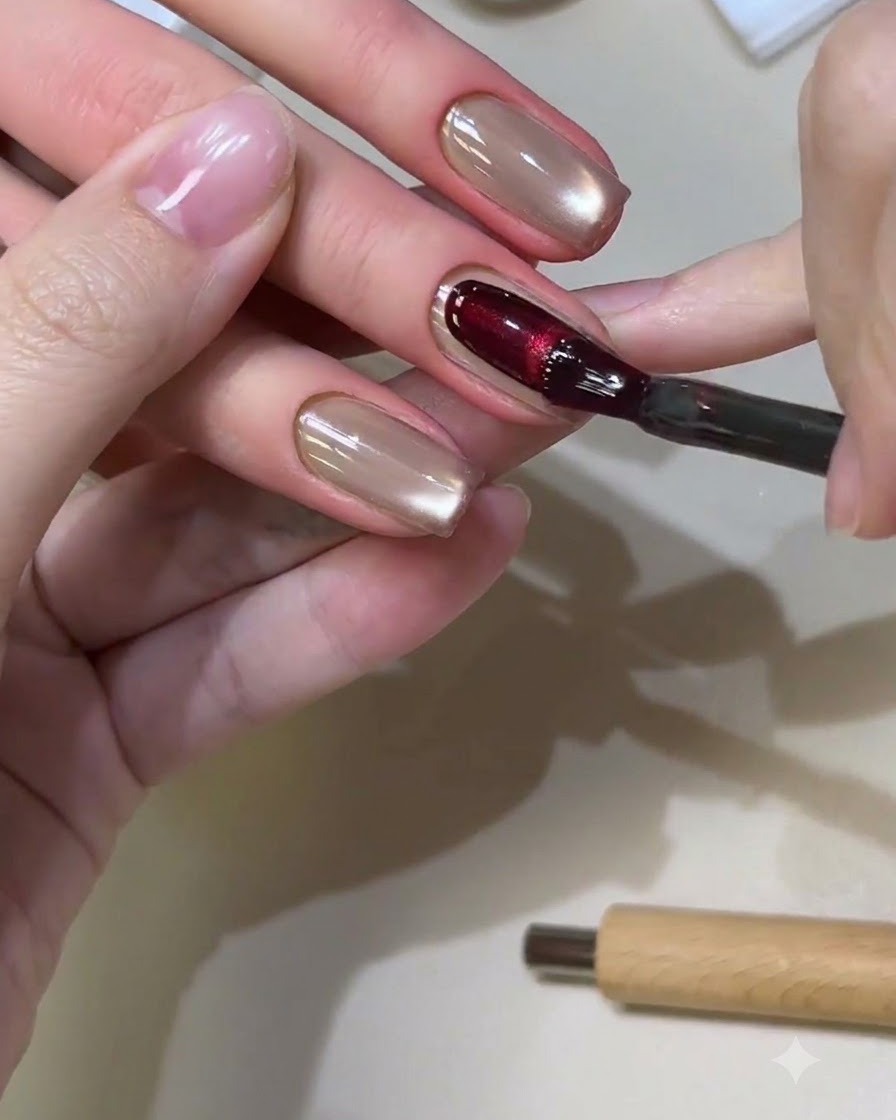 Ein Nagelpinsel trägt ein sattes rotes Cat-Eye-Gel auf einen quadratisch gefeilten Nagel auf.