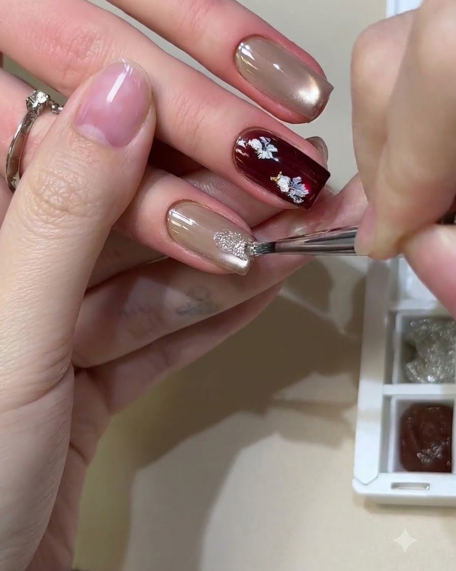 Ein feiner Pinsel tupft glänzende, reflektierende Glitzermaterialien auf einen neutralen Cat-Eye-Gel-Nagel.