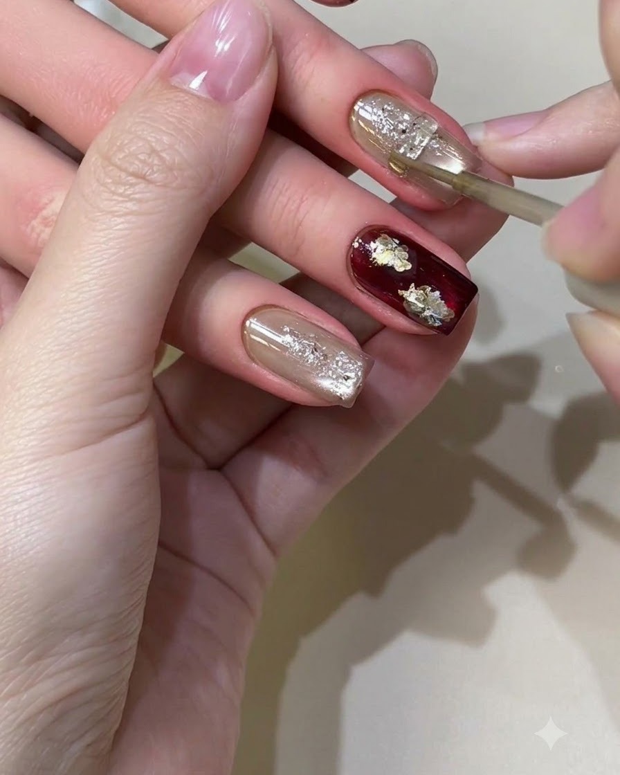 Ein feiner Detailpinsel trägt sorgfältig goldene Metallic-Flüssigkeit auf ein strukturiertes, schimmerndes Nageldesign auf.