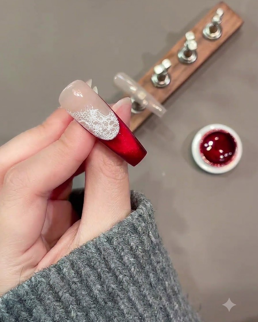 Ein feiner Nail-Art-Pinsel malt lose weiße Rosenkonturen über ein Spitzenmuster auf einem roten und nuden Nagel.