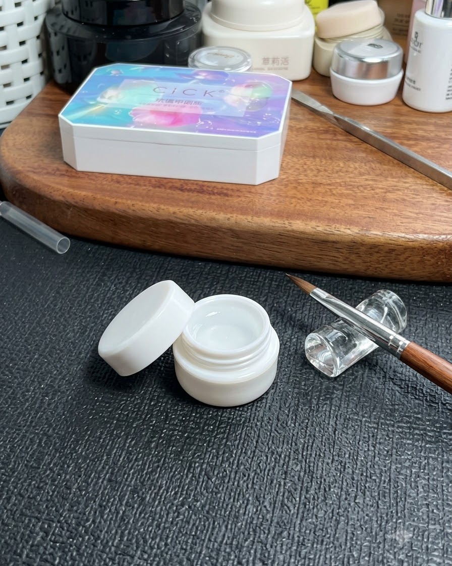 Ein Tiegel mit klarem Basisgel auf einem Tisch neben einem feinen Nageldesign-Pinsel und einer Kosmetik-Aufbewahrungsbox.