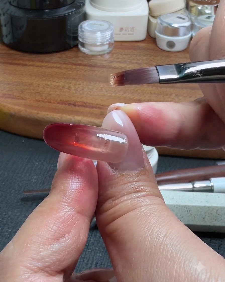 Ein Nagelpinsel nimmt eine winzige Menge Basisgel auf, um es vom roten Block aus nach oben zu ziehen, wodurch ein Ombré-Farbverlauf entsteht.