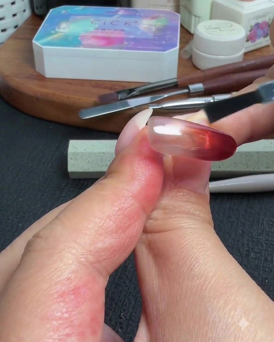 Ein Pinsel trägt einen glänzenden Top Coat über dem fertigen roten Cat-Eye- und Puder-Verlaufsnagel auf.