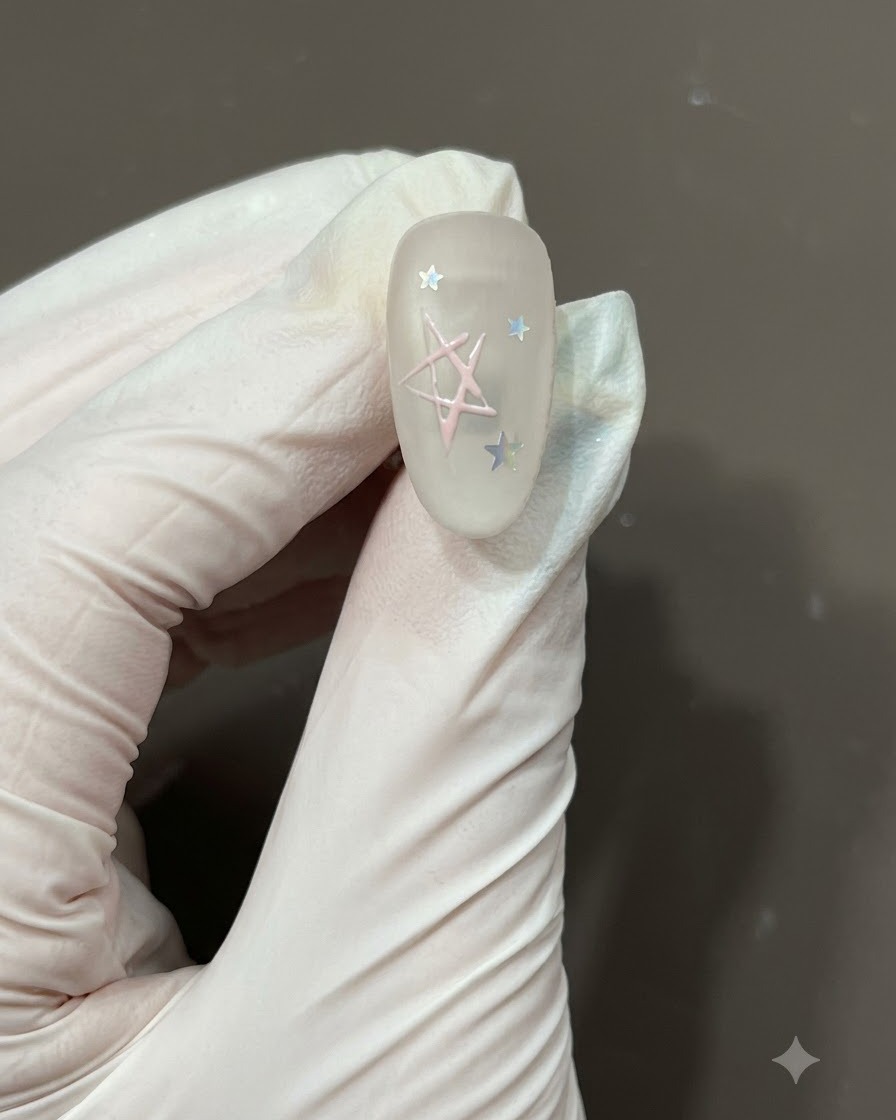 Ein feiner Nail-Art-Pinsel füllt das Zentrum einer handgezeichneten Sternumschrift mit hellrosa Gel-Polish auf einem matten Nagel aus.