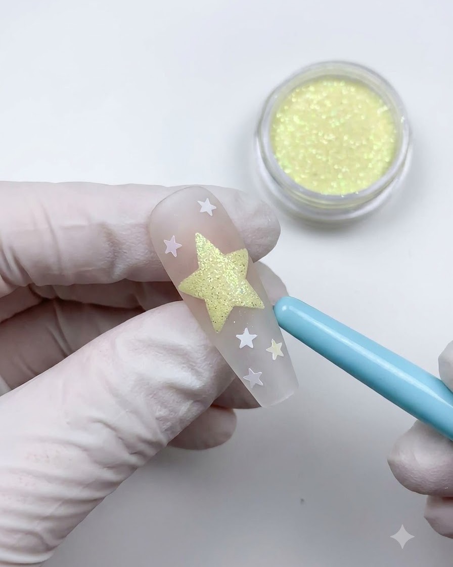 Ein weicher blauer Staubpinsel fegt verbleibendes Pulver weg, um ein strukturiertes Stern-Nail-Art-Design zu offenbaren.