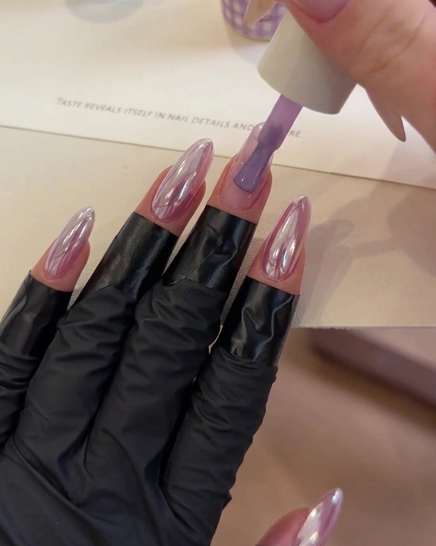 Ein Pinsel platziert einen Tropfen klares Aufbaugel in der Mitte eines lila getönten Fingernagels.