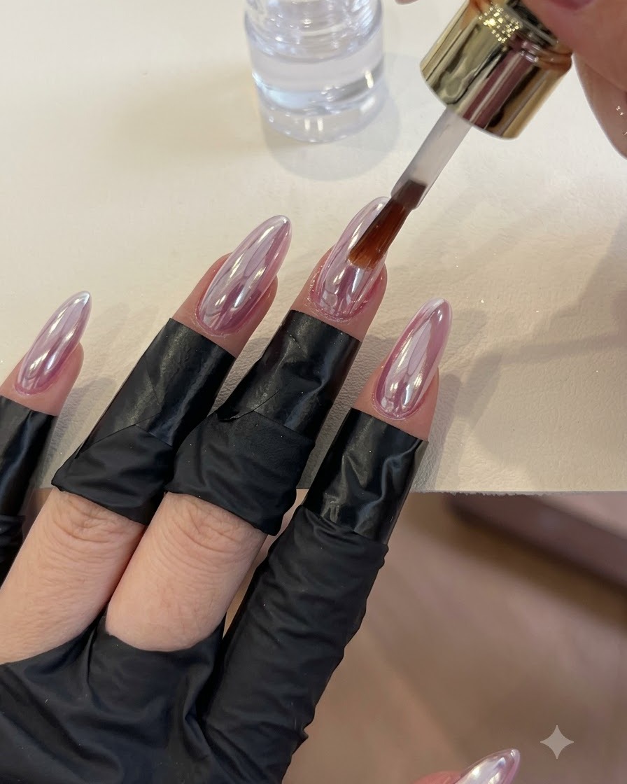 Ein Pinsel trägt klaren Topcoat über glänzende Nägel mit Chrom-Finish auf.