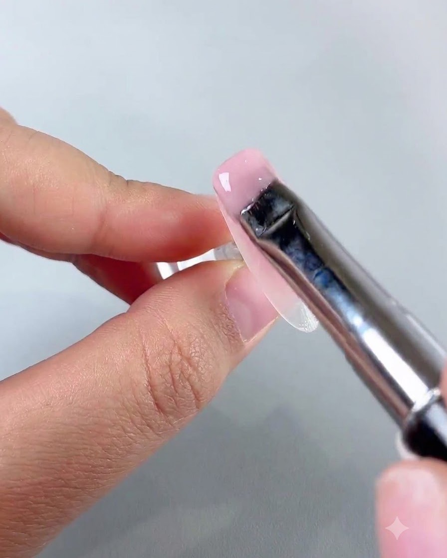 Ein flacher Nail-Art-Pinsel verteilt eine glatte Schicht hellrosa Jade-Basisgel auf der Nageloberfläche.