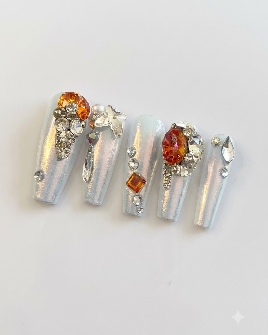Eine Nahaufnahme im Makrobereich, die feine silberne Perlen, kleine Strasssteine und Schmetterlings-Charms auf Press-On Nails gruppiert zeigt.