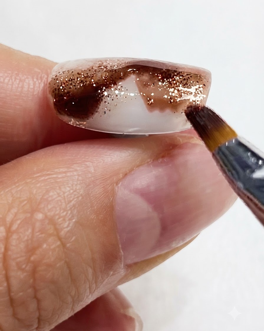 Nahaufnahme eines feinen Pinsels, der bernsteinfarbenes Aquarellpigment nach unten am Nagel entlangzieht.