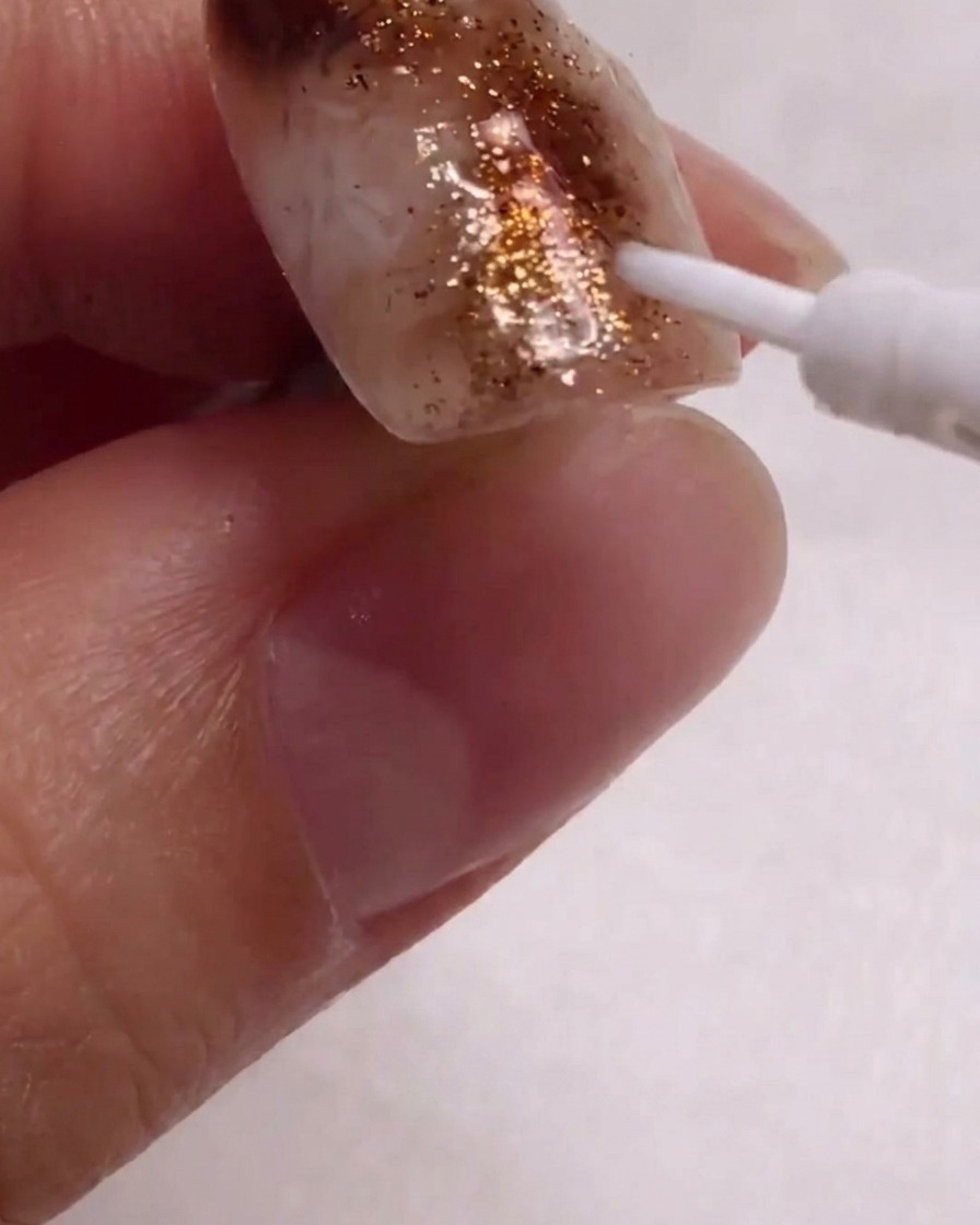 Nahaufnahme eines feinen Linerpinsels, der weiße Details auf das texturierte Nageldesign aufträgt.