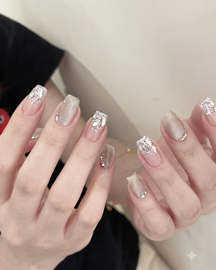 Eine Metallpinzette hält einen funkelnden, klaren Kristall-Strassstein und platziert ihn auf der Basis eines manikürten Nagels.