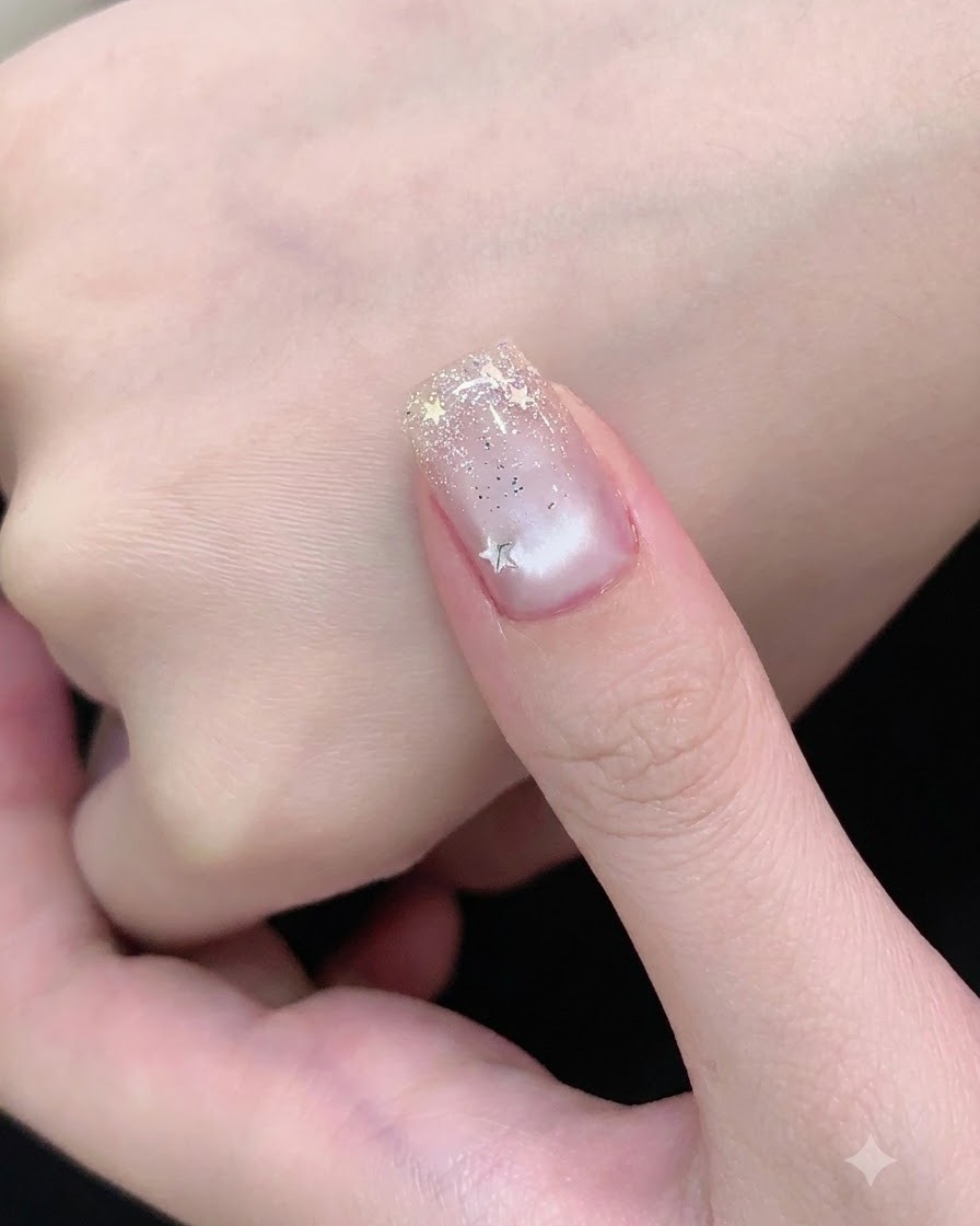 Ein Nagelpinsel trägt einen klaren Versiegelungslack über einen Nagel auf, der mit Silberglitter und Sternen dekoriert ist.