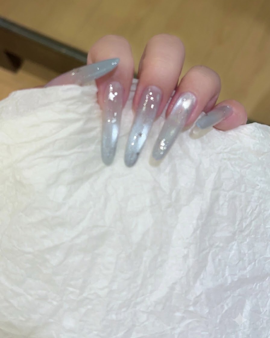 Eine Hand hält ein weißes, strukturiertes Tuch und wischt lange, durchsichtige, mit Gel verlängerte Nägel ab.