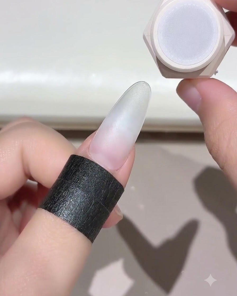 Ein Finger mit einem vorbereiteten Nagel wird neben einem Nagelgel-Gefäß gehalten, bereit zum Aushärten.