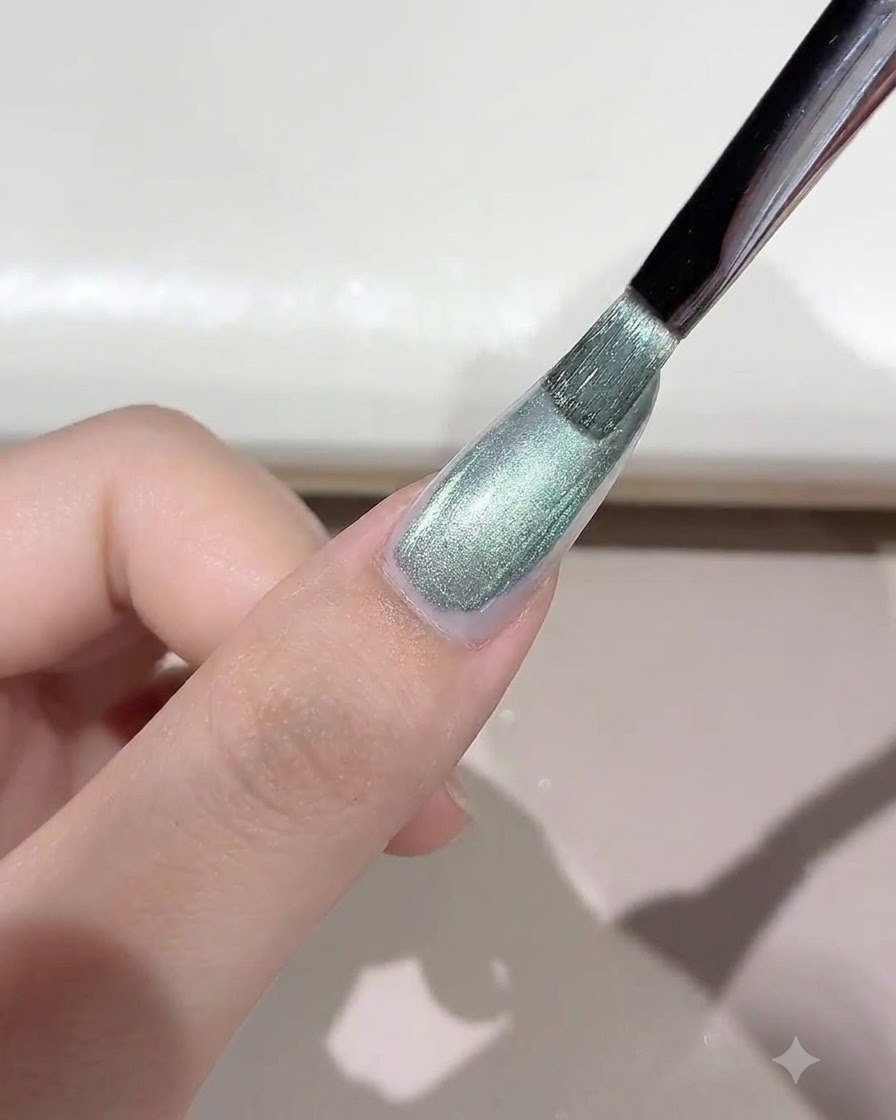 Ein Pinsel trägt schimmerndes, grünlich getöntes Wild-Cat-Eye-Gel auf den Nagel auf.