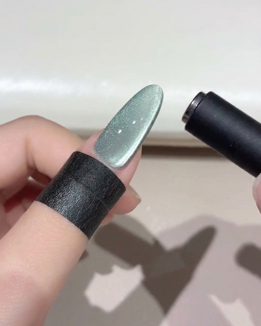 Ein schwarzes Magnetwerkzeug schwebt über einem schimmerten grünen Cat-Eye-Nagel, um das Lichtband zu formen.