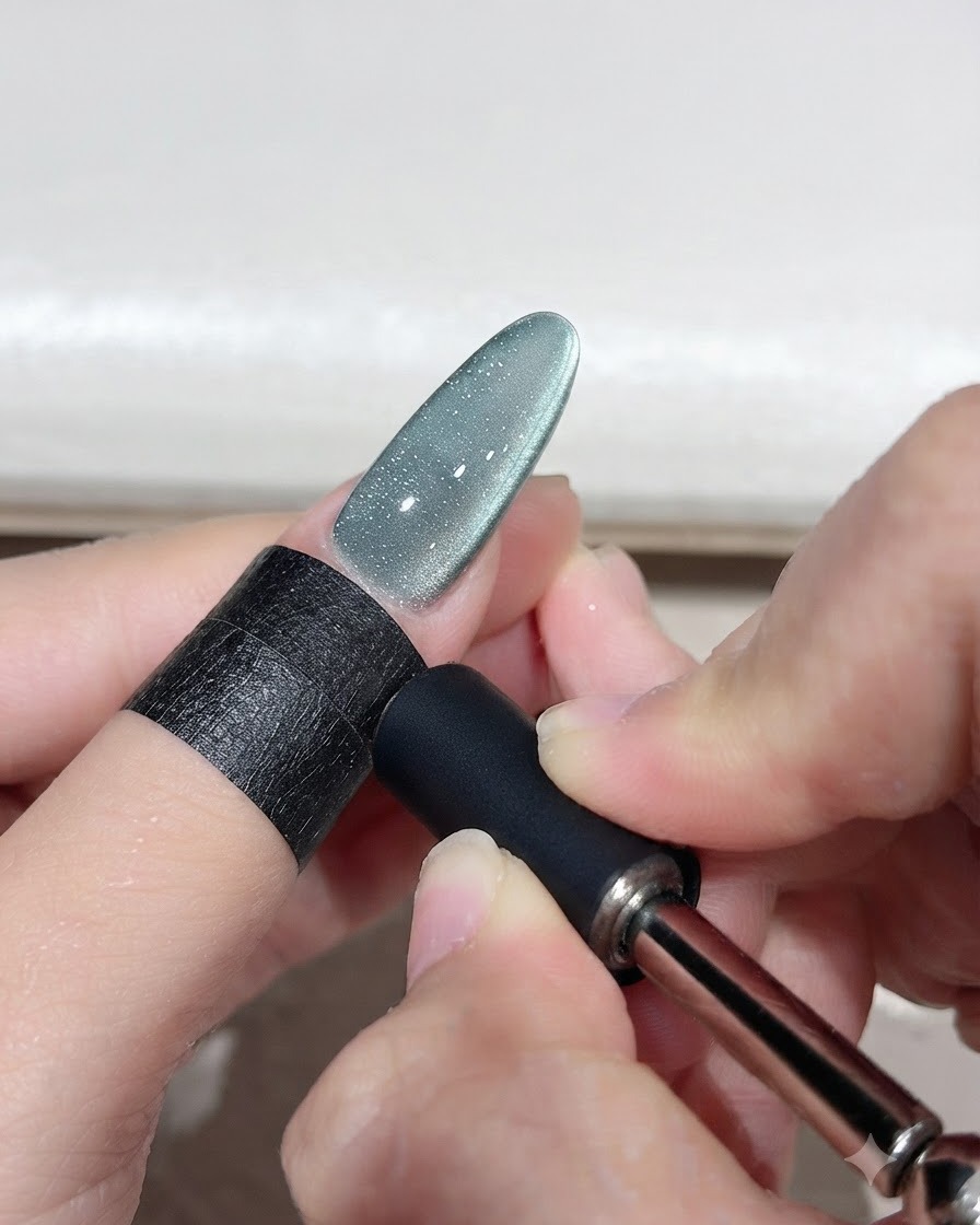 Ein Magnetwerkzeug wird in die Nähe eines grünen Cat-Eye-Gel-Nagels gehalten, um einen geschwungenen Lichtbogen zu formen.