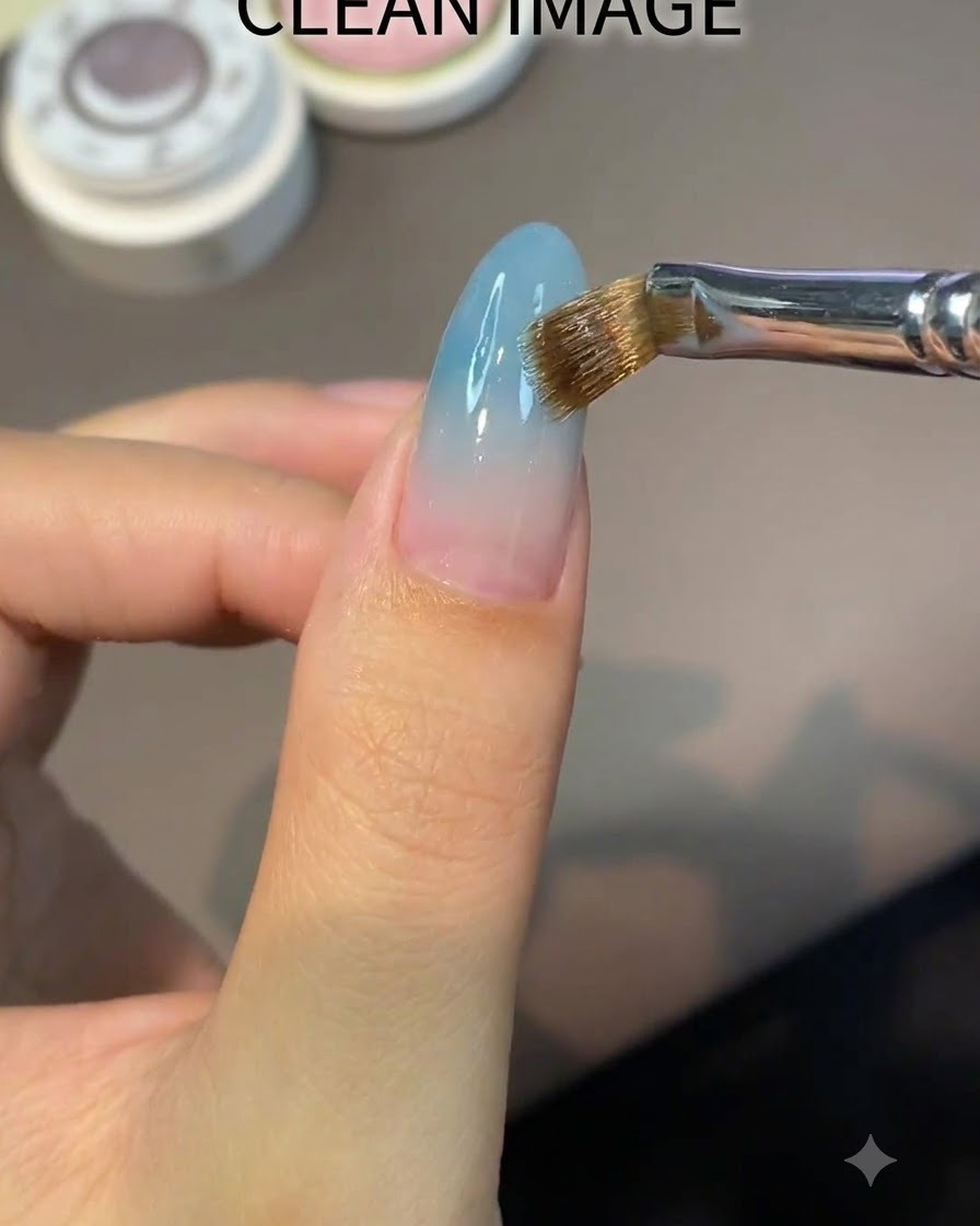 Ein flacher Pinsel trägt gleichmäßig eine klare nude Basisgel-Schicht auf einen mandelförmigen Nagel auf.
