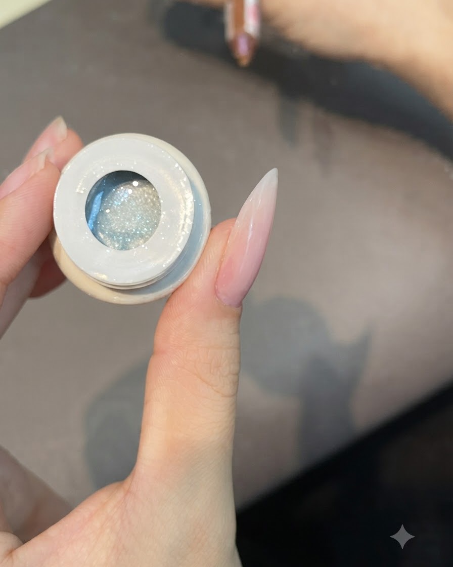 Ein flacher Pinsel taucht in einen offenen Tiegel mit transluzenter Cat-Eye-Gel-Politur Nummer 49 ein.