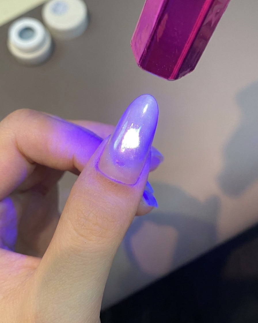 Eine tragbare violette UV-Nagellampe strahlt helles Licht auf einen manikürten Finger, um die Gelschicht auszuhärten.