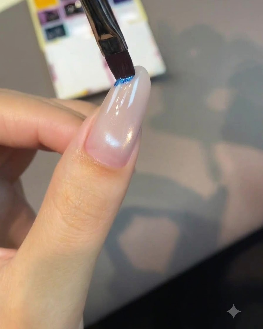 Ein flacher Nail-Art-Pinsel taucht in ein hellblaues Pigmentpfännchen auf einer Palette ein.